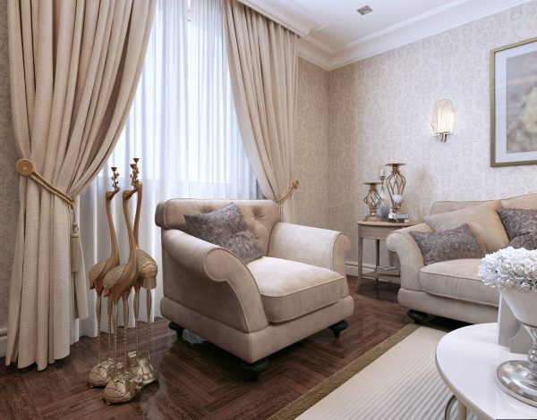 The elegant living room features beige armchairs adorned with decorative pillows, large drapes that cascade gracefully, a rich wooden floor, and charming decorative bird statues. Completing the space is a side table enhanced with stylish ornaments.