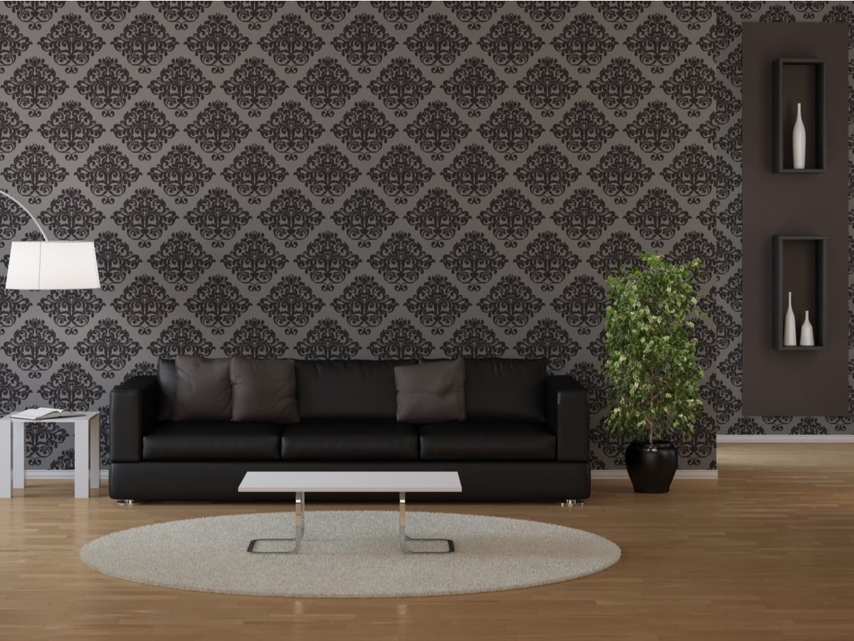 The living room features a black sofa against intricate patterned wallpaper, complemented by a stylish floor lamp, coffee table, and plant. A round rug on the wooden floor adds warmth and texture to this inviting space.