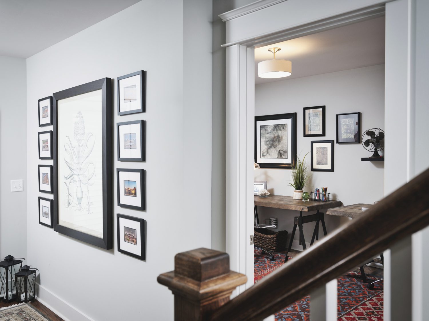 The hallway, adorned with framed art, showcases the do's and don'ts of artwork placement. It leads to a room filled with a desk, art supplies, and more thoughtfully placed pieces. In the foreground, a staircase with a wooden railing invites you to explore further.