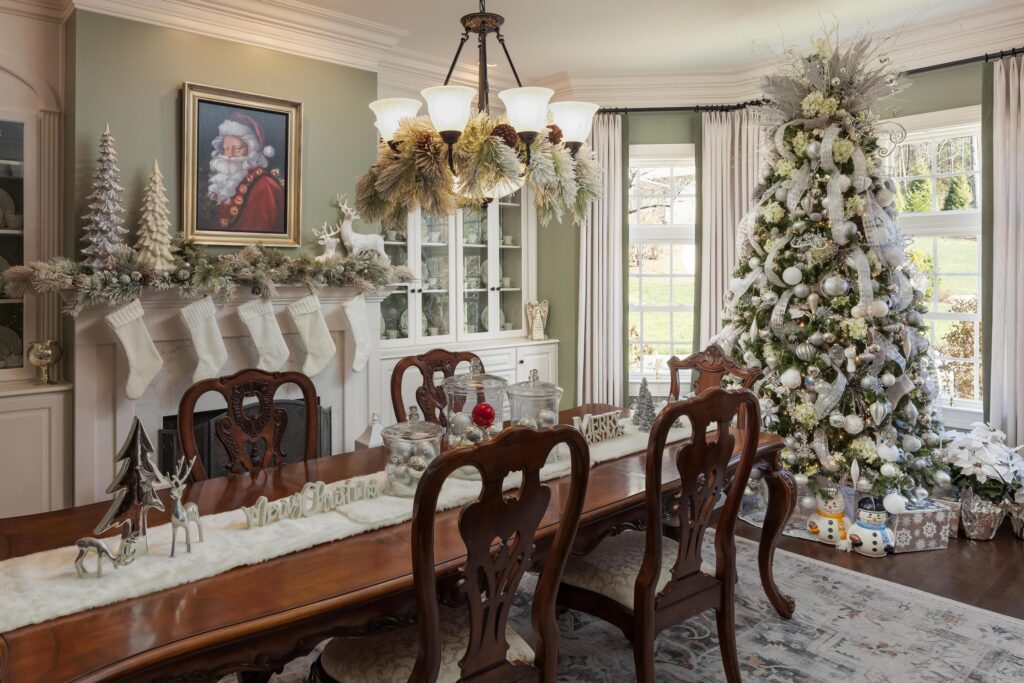 A dining room decorated for Christmas with a tree, stockings on the mantel, a Santa portrait, and festive decor on the table and shelves.